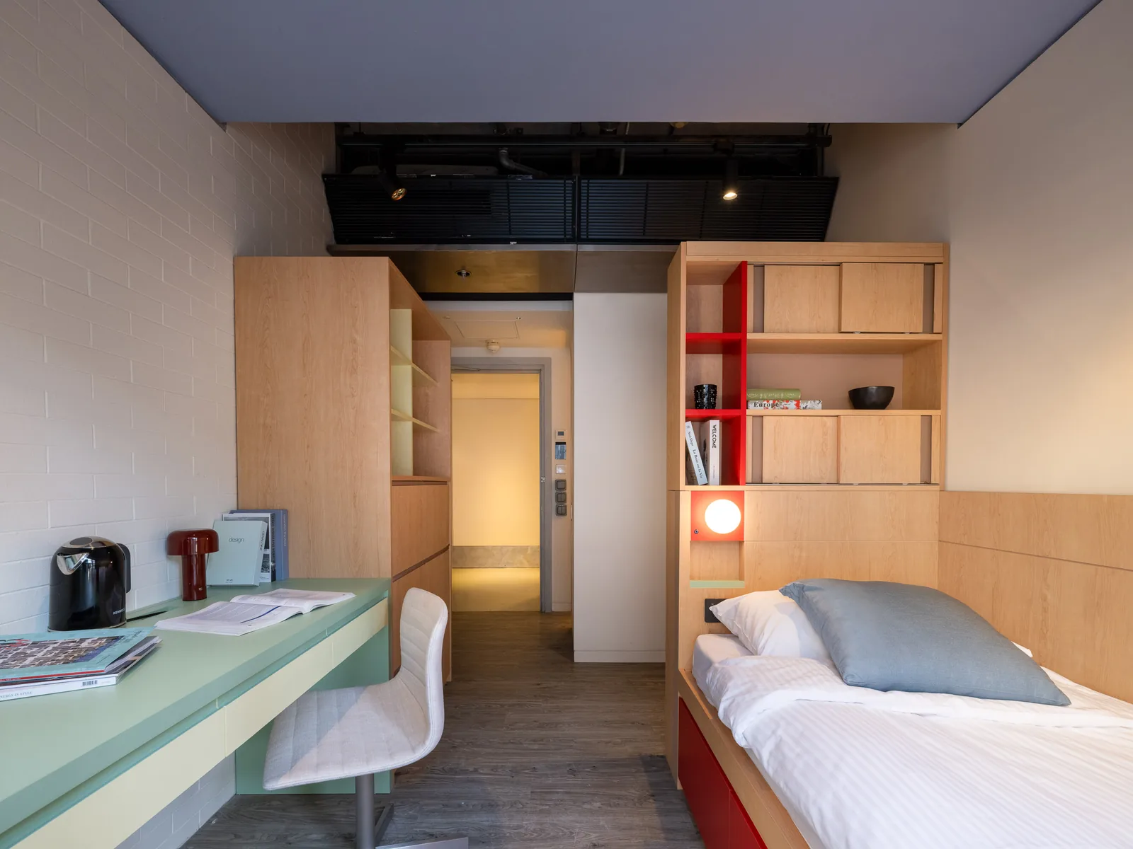 Fully furnished studio room at Stride Wong Chuk Hang, with an oak platform bed, sage-green desk and white brick wall